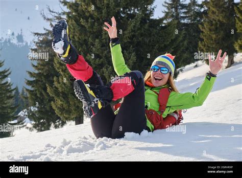 Woman hiker raises her hands and feet and slides down in snow, on her back, on a gentle slope ...