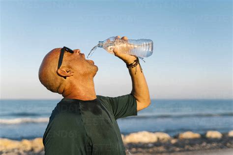 Senior man drinking water while standing against clear sky stock photo