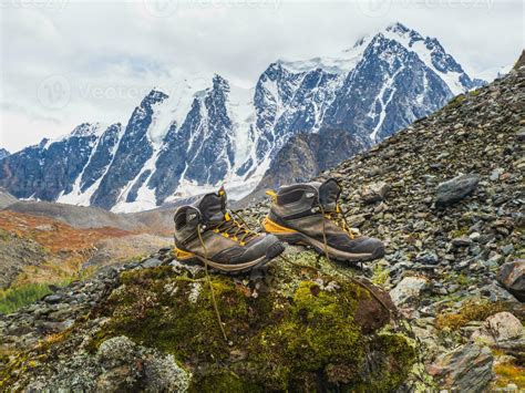 Wet hiking boots dry on a stone against the background of snow-covered high mountains. The ...