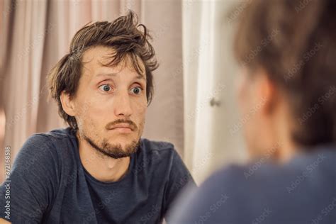 Extremly tired young man looking at himself in the mirror, home alone. self-isolation at home ...