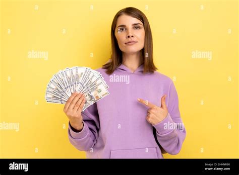 I have big money. Portrait of rich young adult woman pointing at dollar banknotes and looking ...