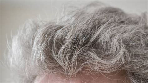 What is the average age at which men typically begin to experience noticeable greying of their hair?