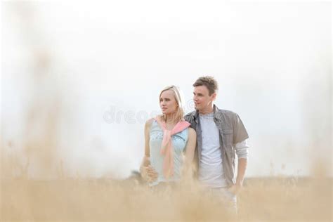 Thoughtful Young Couple Looking Away while Standing at Field Stock Photo - Image of leisure ...
