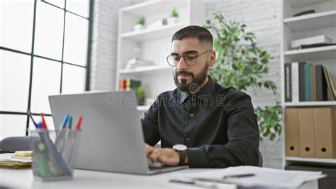 A Focused Bearded Man Working Diligently on His Laptop in a Modern ...