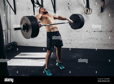 Full length image of tough young man exercising with barbell ...