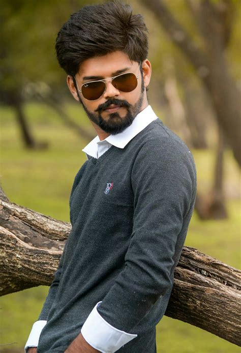 a man wearing sunglasses leaning on a tree branch with his hands in his ...