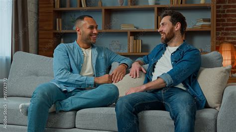 Two diverse 30s men businessmen talking at home on sofa multiracial friends companions african ...