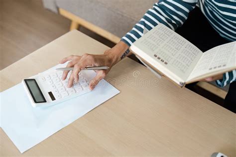 Person Using Calculator and Reading Book at Desk for Financial Planning and Budgeting Stock ...